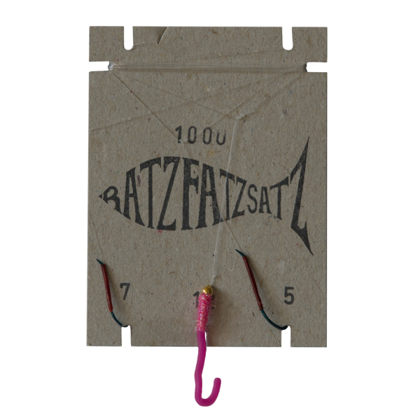 Der RatzFatzSatz 1000 (Pink) ist ein Angelhakenhalter aus Karton mit einer fischförmigen Grafik, zwei daran befestigten Angelhaken, einem rosa Köder und den Zahlen „7“ und „5“ an den unteren Ecken.
