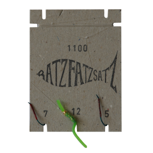 Auf einem quadratischen Karton sind in Fischform „BATZFATZSATZ“ sowie die Nummern 7, 12 und 5 abgebildet, dazu drei Haken – einer davon mit einem Grün-Köder – in Anlehnung an den RatzFatzSatz 1100 (Grün).