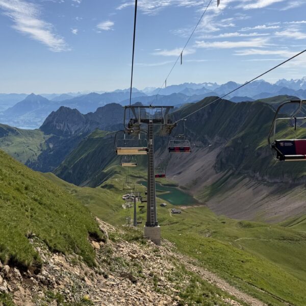 Sesselbahn über grünen Alpen mit Bergsee und Gipfeln