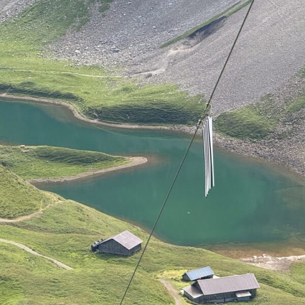 Türkisblauer Bergsee in den Alpen mit grasbewachsenen Hängen und Berghütten