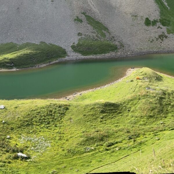 Grüner Bergsee mit Hütte und grasbewachsenen Hängen, Eisee