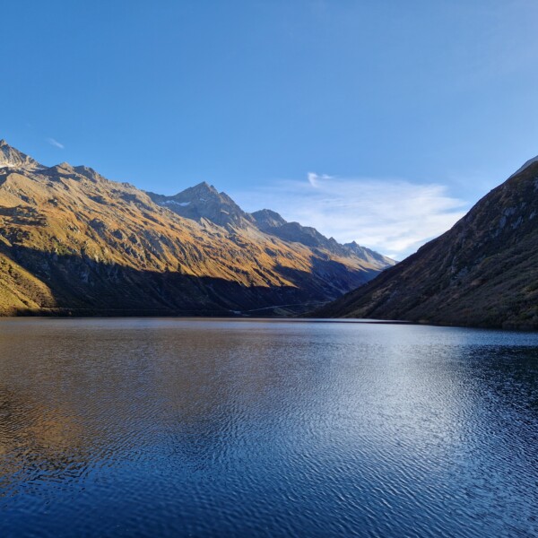 Lai da Nalps: Ruhiger Bergsee mit Spiegelung der umliegenden Gipfel unter blauem Himmel.