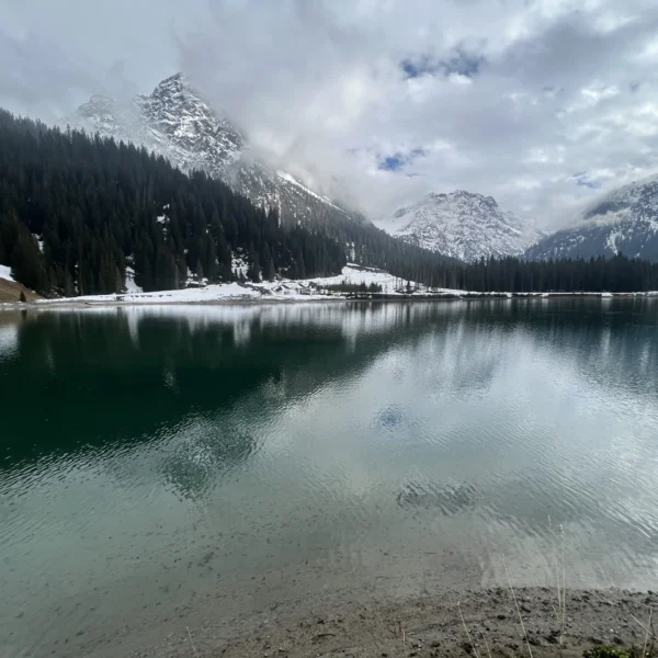 Iselsee mit schneebedeckten Bergen und Nadelwald im Winter