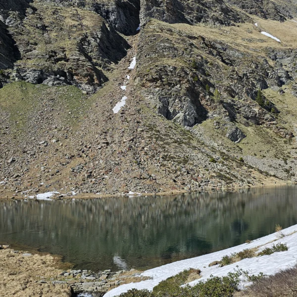 Bergsee Lagh de Calvaresc mit schneebedeckten Hängen und klarem Himmel