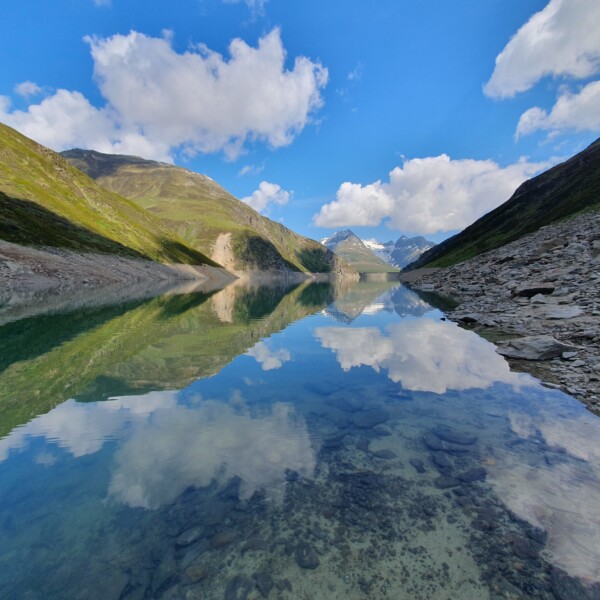 Lai da Curnera: Ruhiger Bergsee mit Spiegelung des Himmels und der Berge.