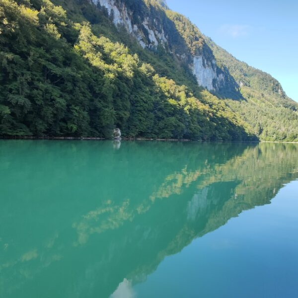 Seelisbergsee: Türkises Wasser spiegelt bewaldete Berge und Felsen im Sonnenlicht.