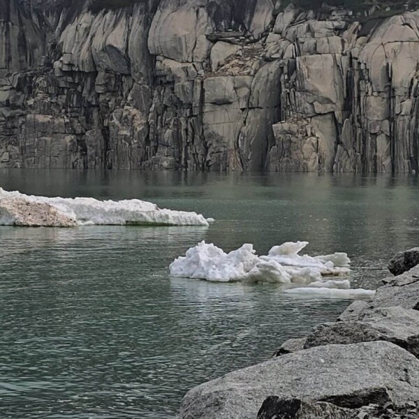 Eisbrocken treiben im grünlichen Wasser nahe dem felsigen Ufer des Göscheneralpsees, einem atemberaubenden Schweizer See. Im Hintergrund erheben sich steile, schroffe Klippen – eine kalte, aber dennoch ruhige Szenerie, perfekt für Wanderfreunde.