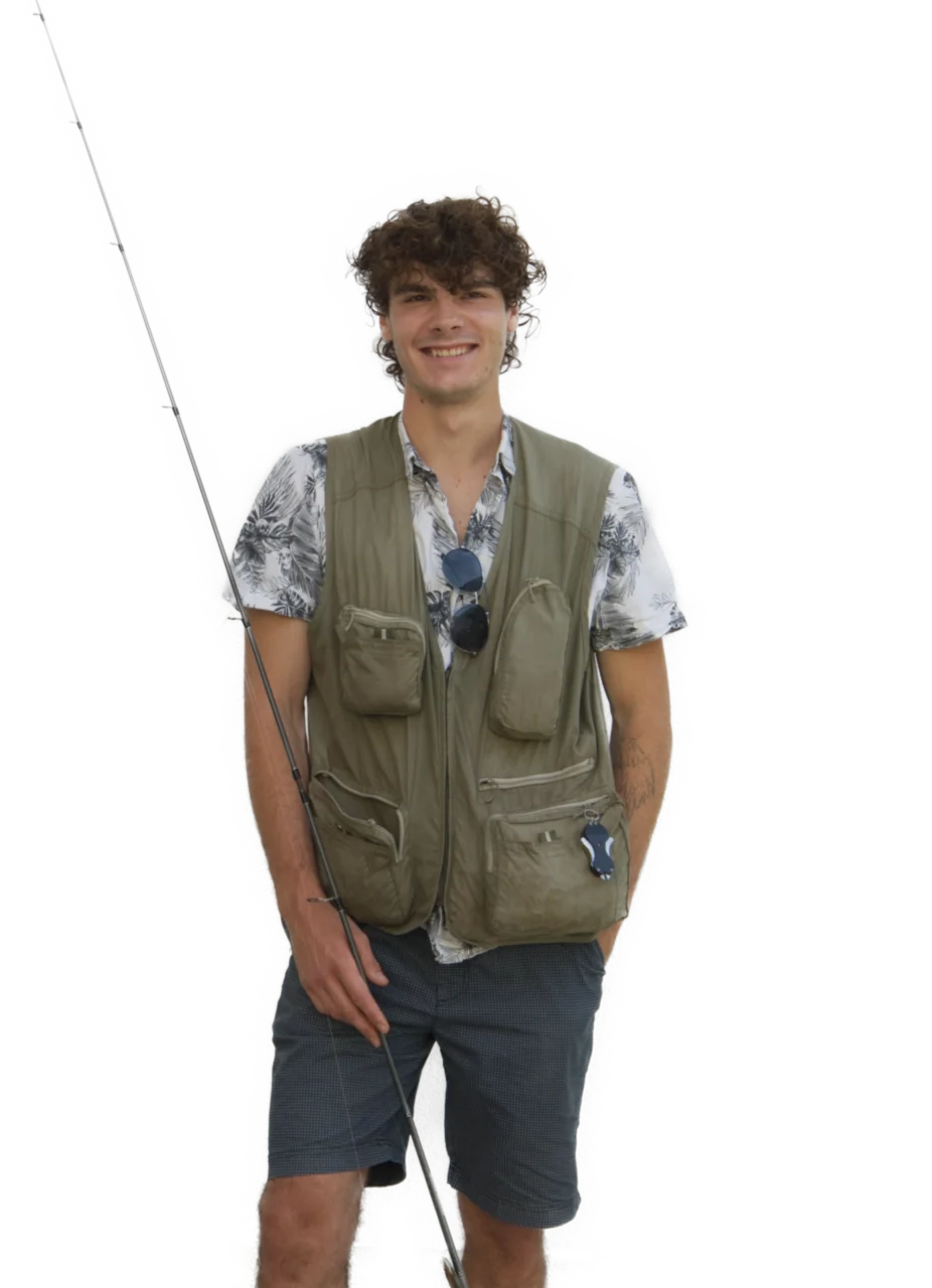 Ein junger Mann in Anglerweste, gemustertem Hemd und Shorts steht mit einer Angelrute in der Hand da. Er lächelt und an seiner Weste hängt eine Sonnenbrille.