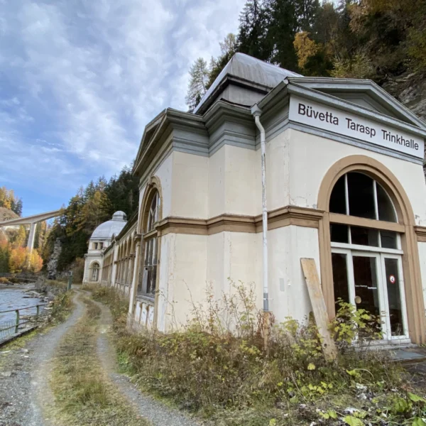 Büvetta Tarasp Trinkhalle am Inn mit Brücke im Hintergrund.