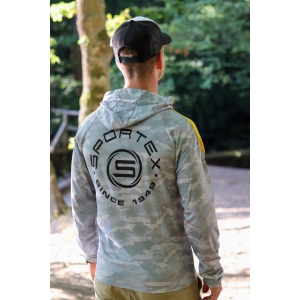 Eine Person, die ein Sportex UV Shirt gelb/grau camou (Größe M) und eine schwarze Mütze trägt, steht im Freien mit dem Rücken zur Kamera, umgeben von Grün und Sonnenlicht.