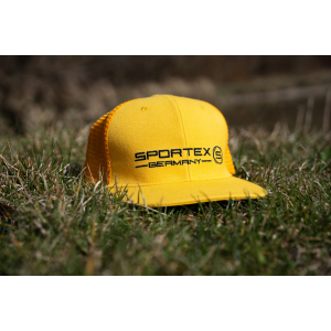 Ein Sportex gelbes Snap Cap Mesh 6 Panel // Stick mit "Sportex Germany" in schwarzer Schrift liegt im Freien auf grünem Gras und glänzt im Sonnenlicht.