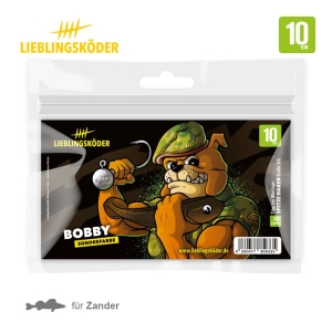 Die Bobby 10cm Angelköder-Verpackung zeigt einen muskulösen Cartoon-Hund in Armeeausrüstung mit einem Angelhaken. Die Aufschrift "Bobby", "10 cm" und "für Zander" ist in den Farben Schwarz, Grün und Orange gehalten.
