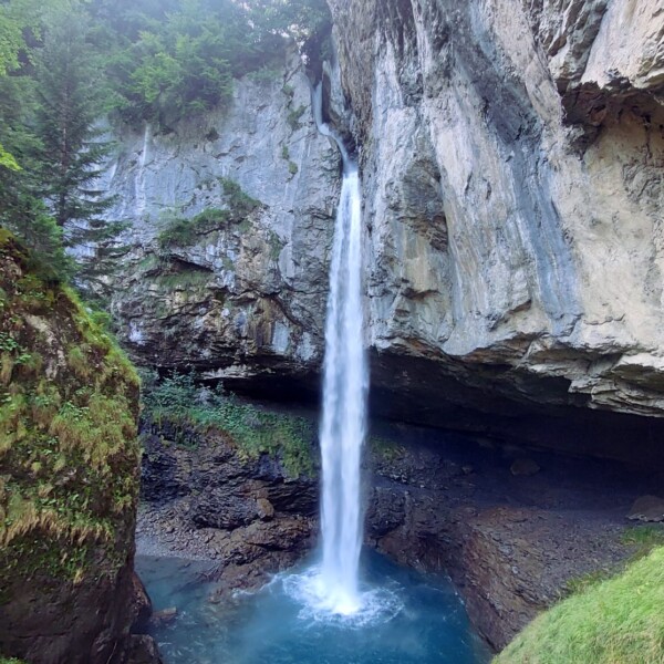 Fätschbach Wasserfall stürzt in ein blaues Becken, umgeben von Felsen und Grün.