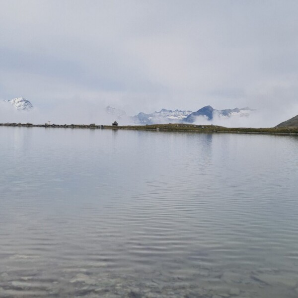 Illsee: Ruhiger Bergsee mit Spiegelung und verschneiten Gipfeln im Hintergrund.