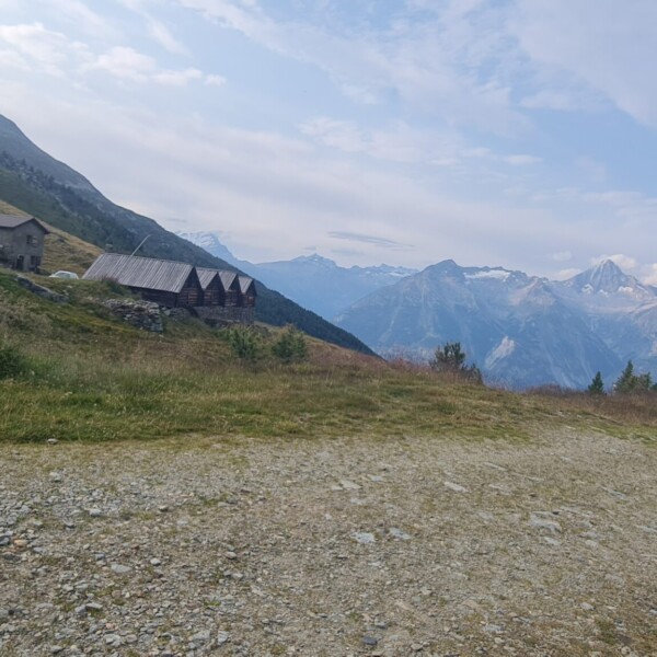 Illsee: Berglandschaft mit Hütten und einem Schotterweg vor schneebedeckten Gipfeln.