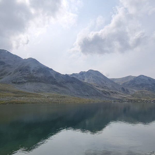 Illsee: Bergsee mit Spiegelung der Berge unter bewölktem Himmel.