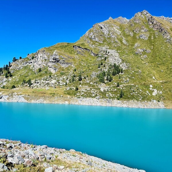 Türkisblauer Lac de Cleuson vor Bergkulisse unter strahlend blauem Himmel.