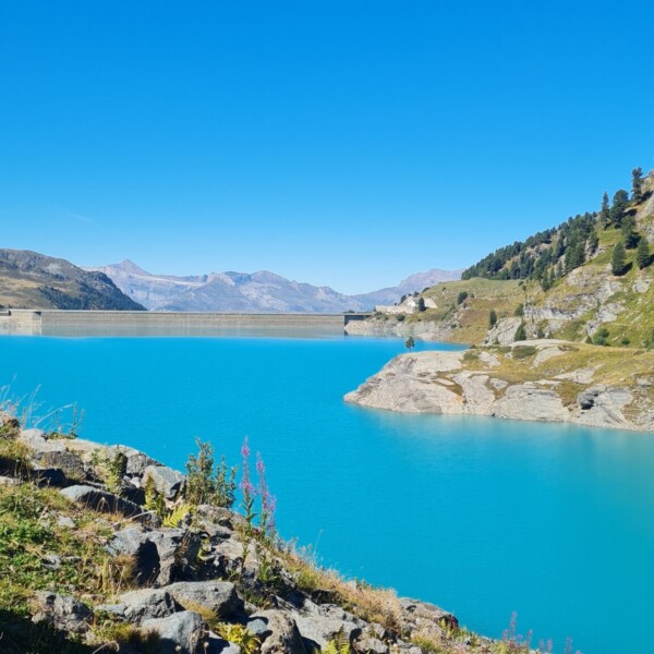 Türkisblauer Lac de Cleuson mit Staumauer und Berglandschaft unter strahlend blauem Himmel.