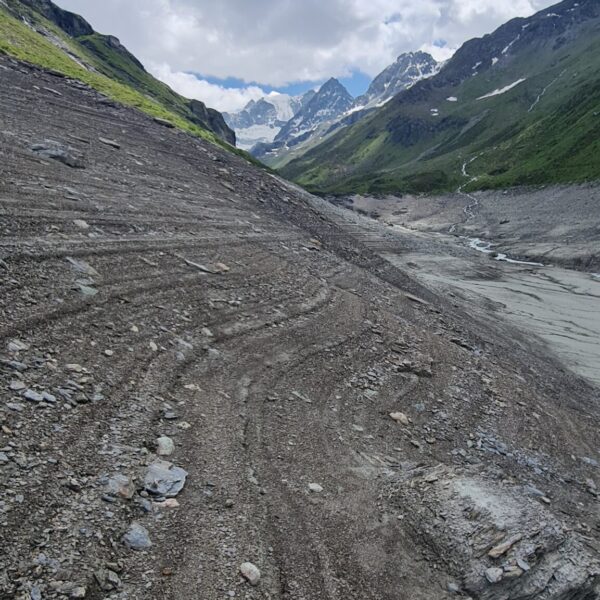 Geröllfeld am Lac de Moiry mit Blick auf schneebedeckte Berge und blauen Himmel.