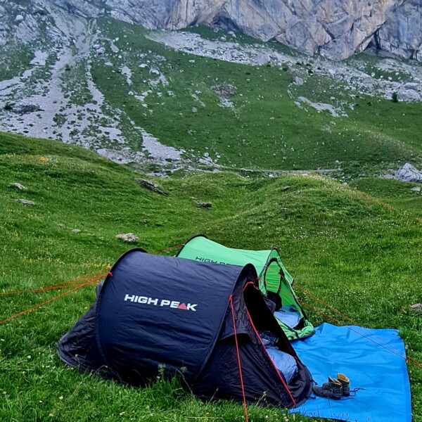 Zwei High Peak Zelte auf einer grünen Wiese in der Nähe des Sanetschsees, mit Bergen im Hintergrund.