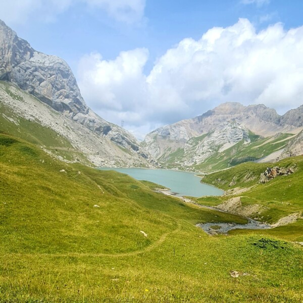 Sanetschsee: Türkisfarbener Bergsee in grüner Alpenlandschaft mit bewölktem Himmel.