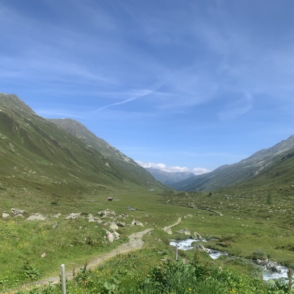 Grüne Schlappinbach-Talansicht mit Bachlauf und Bergen unter blauem Himmel.