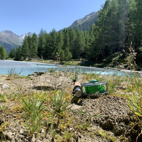 Fliegenfischen-Rolle am Susasca-Fluss in den Schweizer Alpen vor Bergpanorama.