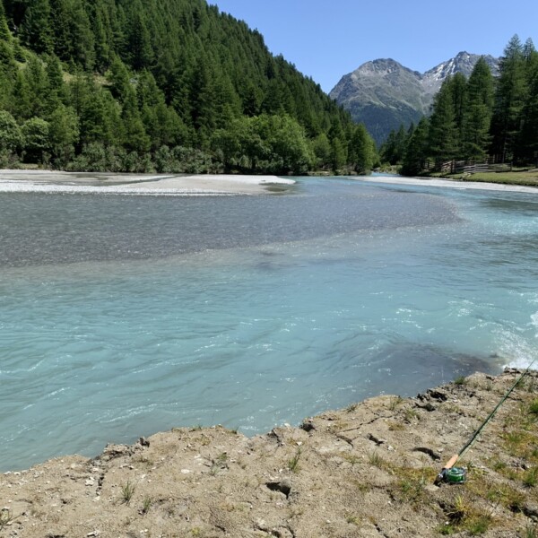 Türkisfarbener Fluss Susasca in einer grünen Berglandschaft mit schneebedeckten Gipfeln.
