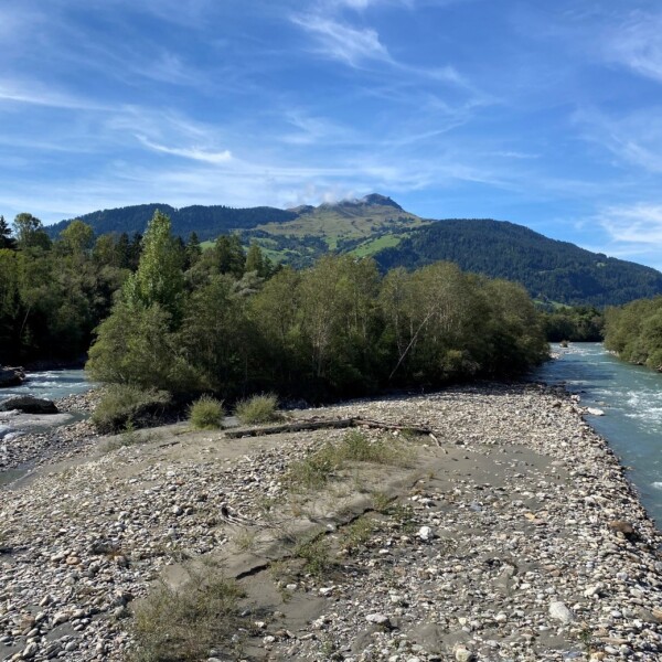 Vorderrhein Flusslandschaft mit Bergkulisse unter blauem Himmel.