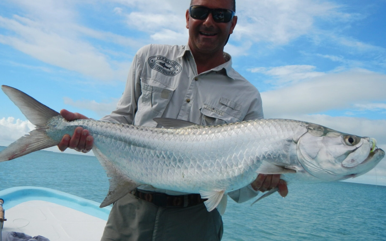 Mann hält stolz einen großen Tarpon, gefangen beim Angeln im Urlaub.