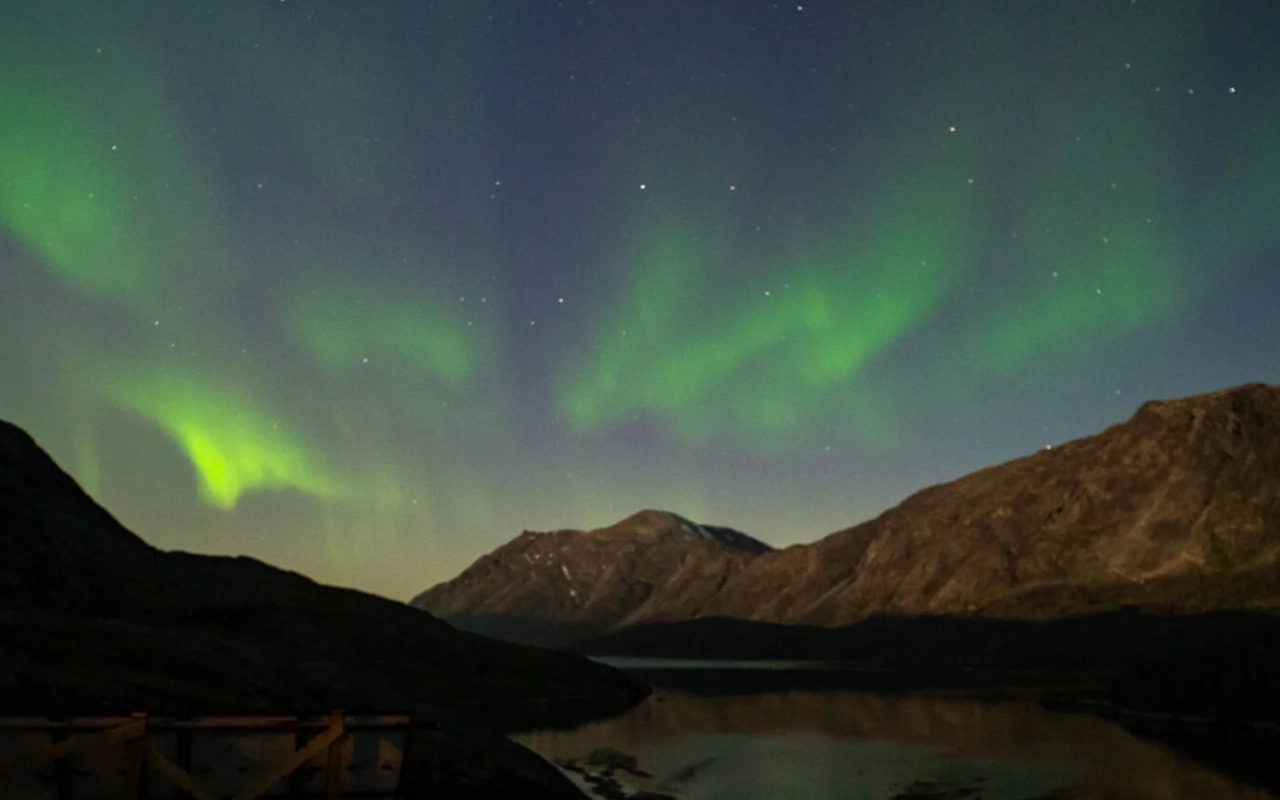 Nordlichter über Bergen und einem See. Atemberaubende Ferien- & Reise-Szene.