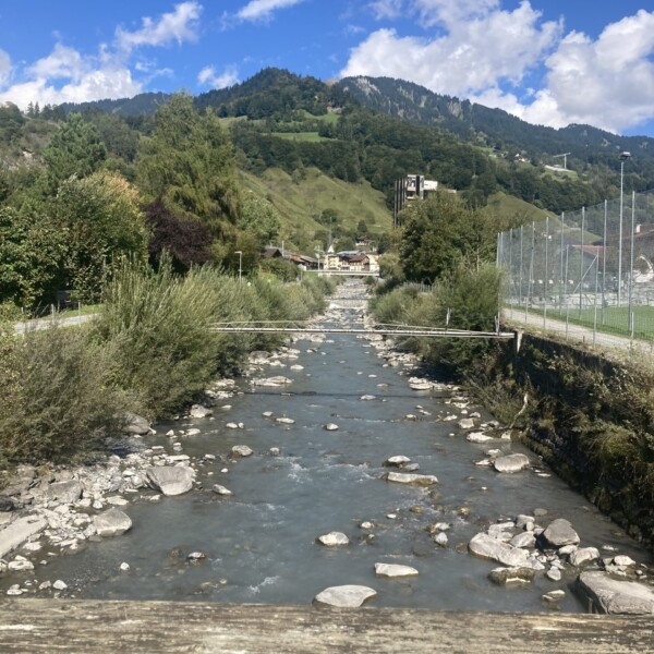 Taschinasbach Fluss mit Bergen im Hintergrund, grüne Landschaft.