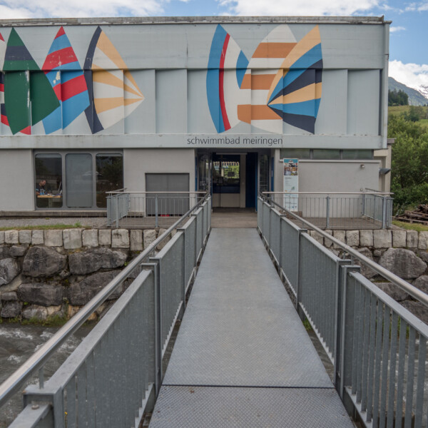 Schwimmbad Meiringen Eingang mit Brücke über den Fluss. Bunte Fassadengestaltung.