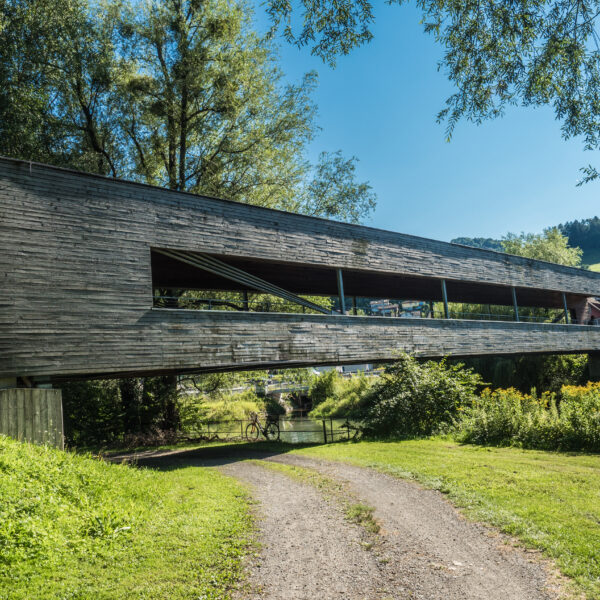 Moderne Holzbrücke über den Alten Rhein, umgeben von Grün.