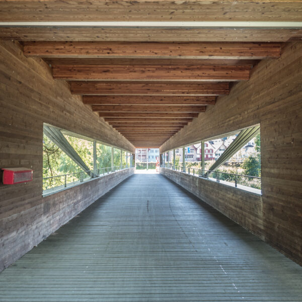 Holzbrücke Alter Rhein mit Blick auf Häuser und Bäume. Überdachter Fußweg.