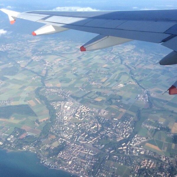 Flugzeugflügel über Asse, Schweiz, mit Feldern und Stadtansicht.