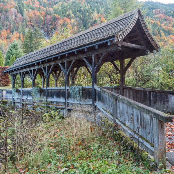 Gedeckte Holzbrücke im Herbst mit bunten Bäumen im Hintergrund. Avançon.