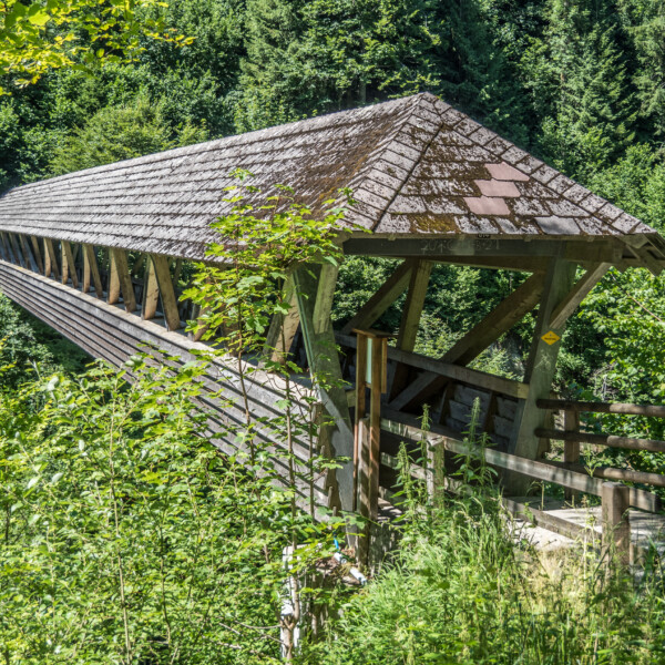 Überdachte Holzbrücke im Badtobelbach, umgeben von üppigem Grün.