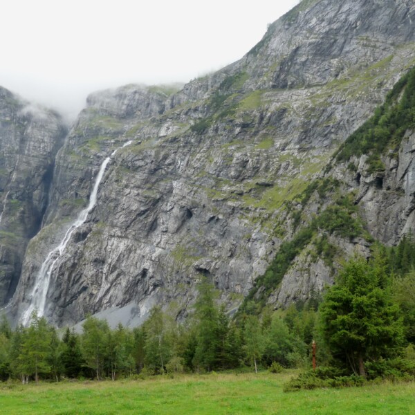 Balmhornbach: Wasserfall an steiler Felswand, umgeben von grünen Bäumen und Wiesen.