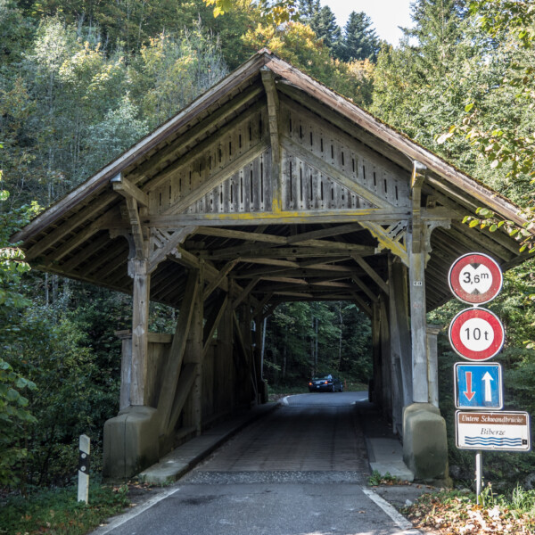 Gedeckte Holzbrücke Biberze mit Verkehrsschildern und Auto im Hintergrund.