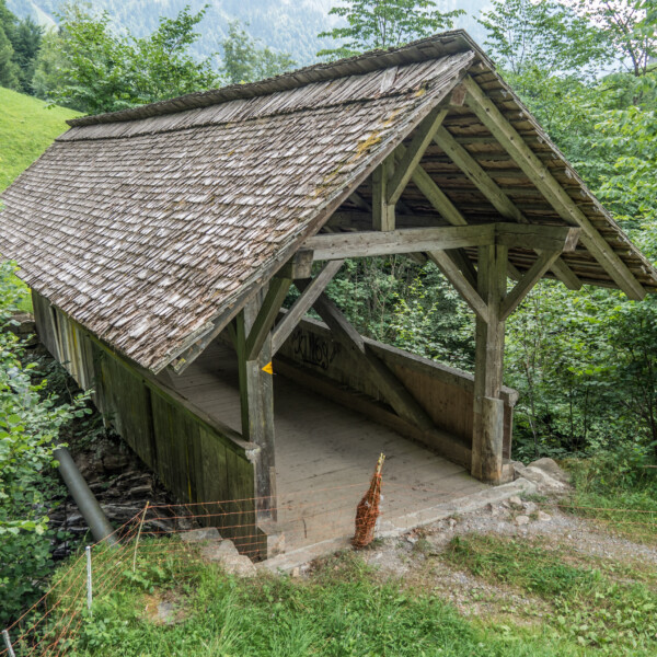 Gedeckte Holzbrücke über den Bolbach, umgeben von üppigem Grün.