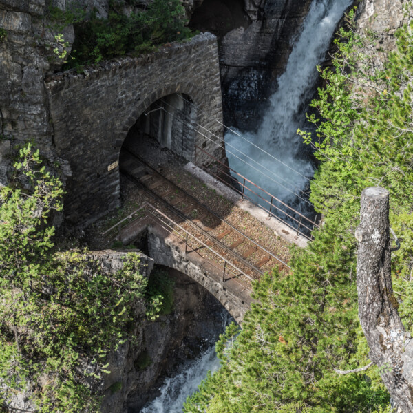 Brüggentobelbach: Eisenbahnbrücke mit Tunnel und Wasserfall, eingebettet in Felsen und Vegetation.