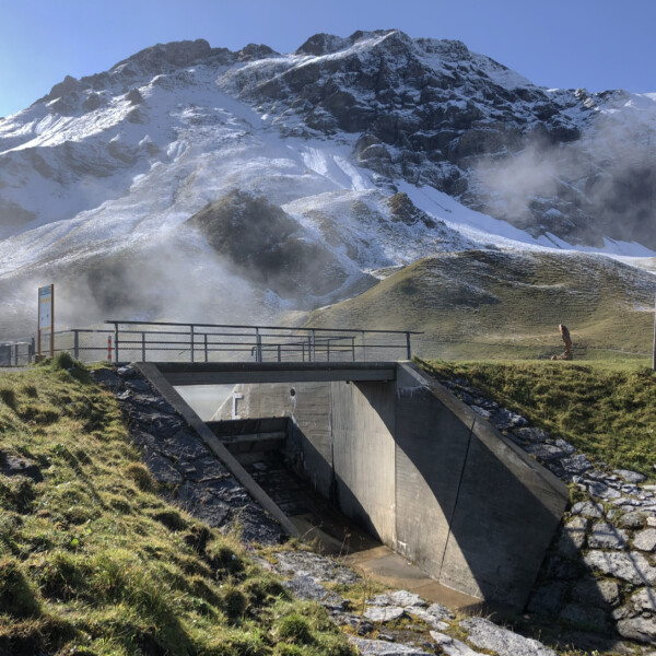 Brücke über den Cheselenbach (Melchsee) mit schneebedeckten Bergen im Hintergrund.