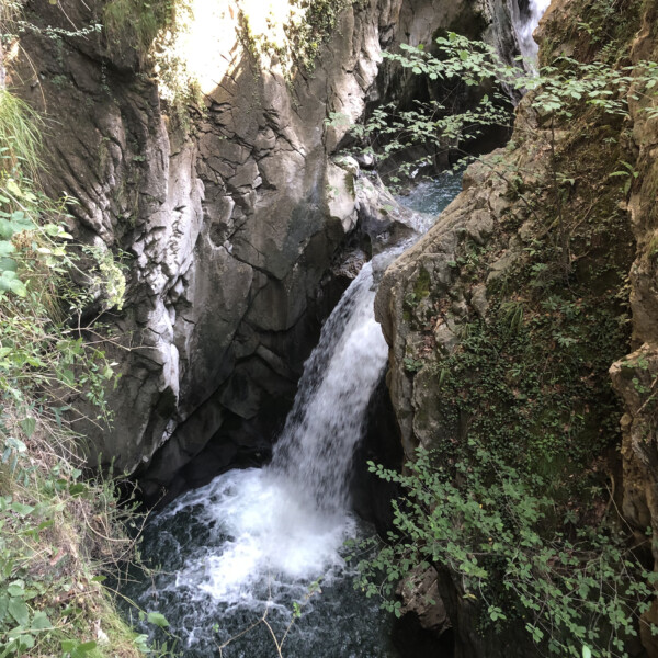 Wasserfall im Choltalbach, Emmetten, stürzt in eine tiefe Schlucht. Grüne Vegetation umgibt das felsige Gelände.