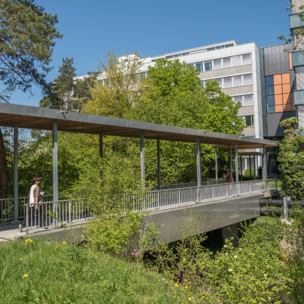 Überdachte Brücke in Chriesbach verbindet Gebäude, umgeben von Grün.