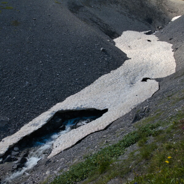 Schneefeld über dem Ducanbach-Bachbett in einer alpinen Landschaft.