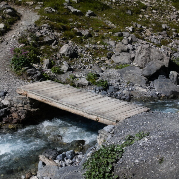 Holzbrücke über den Ducanbach, umgeben von Felsen und Grün. Wanderweg.