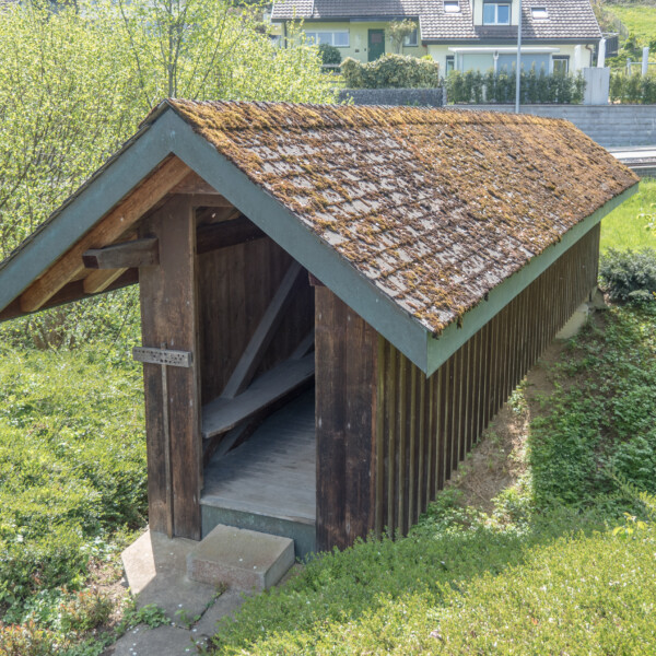 Holzschuppen mit Moosdach am Esslingerbach, eingebettet in Grün.