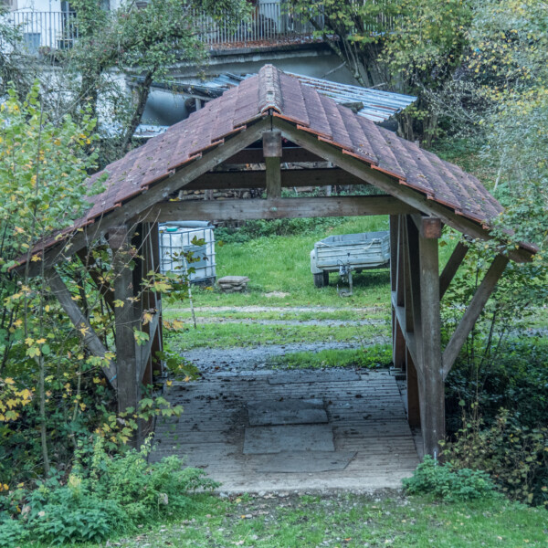 Überdachte Holzbrücke über den Etzgerbach. Ländliche Szene mit Grün.
