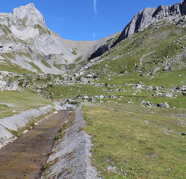Glattalpseebach-Kanal vor alpiner Landschaft mit Bergen und grünen Wiesen.